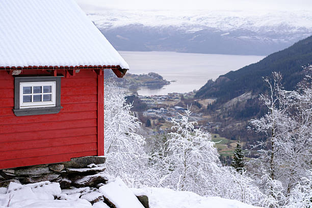 A perfect Christmas destination in a cozy red cabin in winter, in a snowy forest with the Hardanger Fjord in the background, in Norheimsund, Norway.