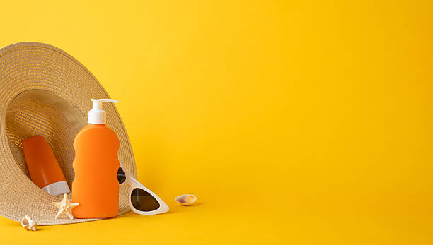 Sunscreen, sunglasses, a hat, and a starfish displayed against a bright yellow backdrop, evoking summer travel and sun protection. Perfect imagery for vacation and summer-themed matters