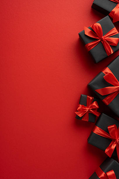 istock Various vertical black gift boxes with bright red ribbons arranged on a vivid red surface 2226536949