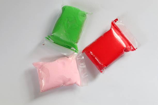 Three individually wrapped packs of bright red, green and pink modeling clay on a white backdrop. An ideal resource for children's arts and crafts themes.
