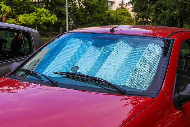 Bright red compact car with sun protection windshield cover parked outdoors on summer day