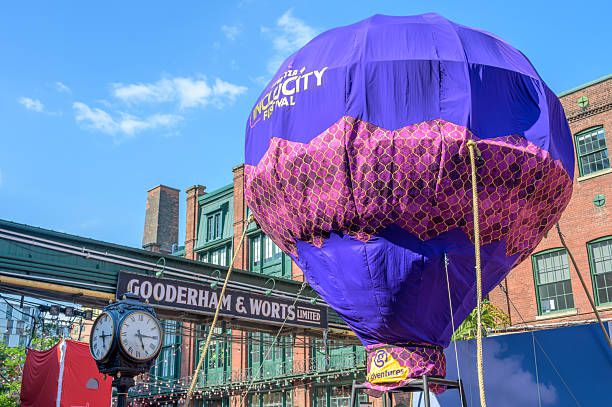 Toronto, Canada - July 13, 2025: Purple inflatable balloon with IncluCity Festival branding rises near the Gooderham and Worts sign, with a vintage clock and brick buildings in the Distillery District.