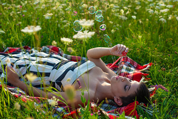 Beautiful young woman having fun on the meadow, blowing soap bubbles on a sunny summer day.
