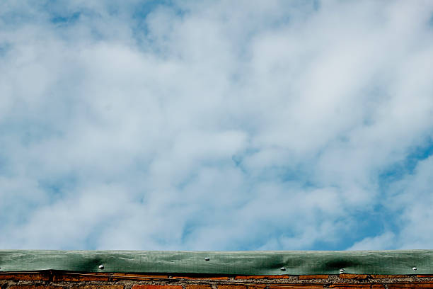 beautiful clear sky with white clouds, captured above a weathered brick wall with a green material atop.