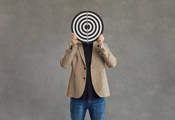 istock Unknown businessman hid his face behind a darts board while standing on a gray background. 2226546957