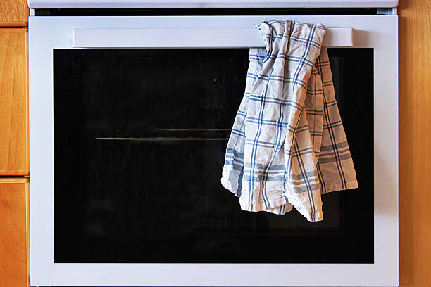 The front view of a white kitchen oven with control knobs and a plaid kitchen towel hanging from the handle.
