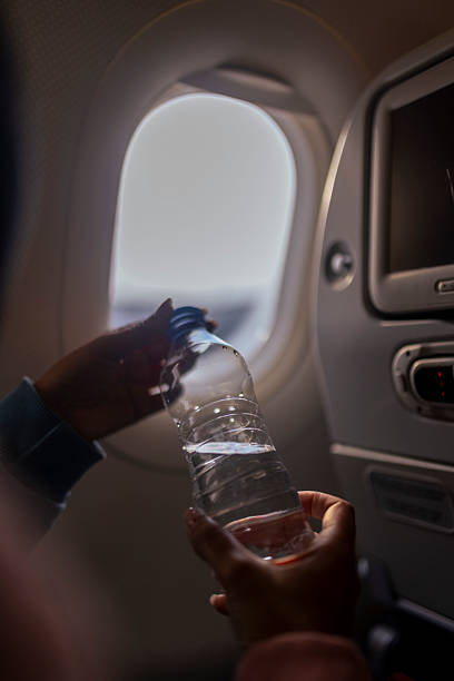 istock Passenger's perspective of opening a plastic water bottle during an airplane flight, next to the window and entertainment screen 2226556084
