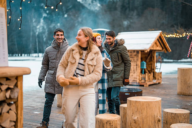 istock Two Couples Laughing at Winter Resort with Cozy Cabin Background 2226557553