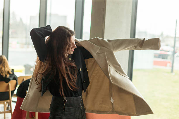 istock A woman is trying on a stylish coat while standing in front of a window 2226562490