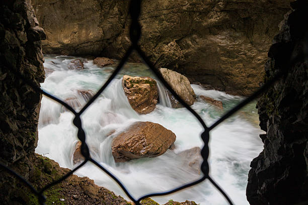 View through a safety fence at the rushing turquoise waters inside Partnachklamm Gorge, Garmisch-Partenkirchen, Bavaria. A dramatic look at nature's raw force through a secure walking trail.