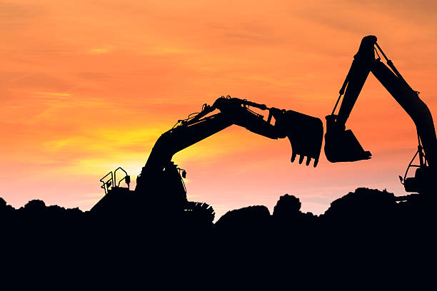 istock Two Excavators silhouette are digging soil with bucket lift up 2226566664