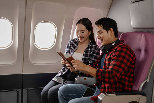 istock Asian couple sitting together on an airplane, smiling while looking at documents. They appear happy and excited about traveling, dressed casually with a bright airplane cabin in the background. 2226574444