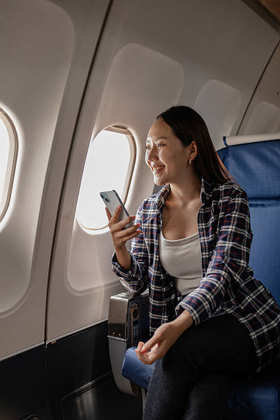 istock Asian woman smiling while using her smartphone on an airplane. She is sitting next to the window, enjoying her time during the flight. The atmosphere appears relaxed and comfortable. 2226574711