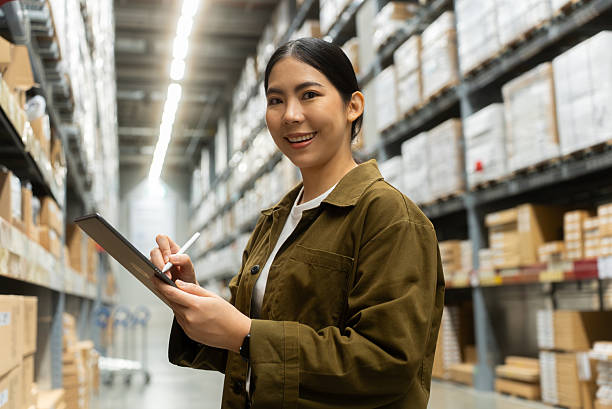 istock Portrait smiling confidently woman worker managing track inventory to fulfill data using smart digital tablet in logistics center with stacked shipping boxes and supply chain products in warehouse. 2226575316