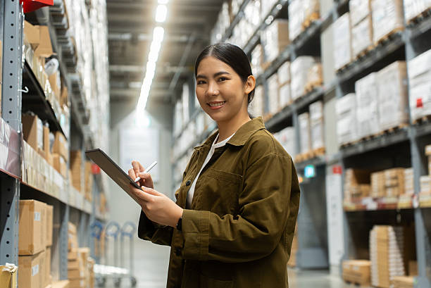 istock Portrait smiling confidently woman worker managing track inventory to fulfill data using smart digital tablet in logistics center with stacked shipping boxes and supply chain products in warehouse. 2226575368