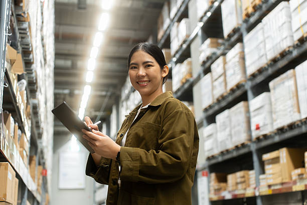 istock Portrait smiling confidently woman worker managing track inventory to fulfill data using smart digital tablet in logistics center with stacked shipping boxes and supply chain products in warehouse. 2226575369