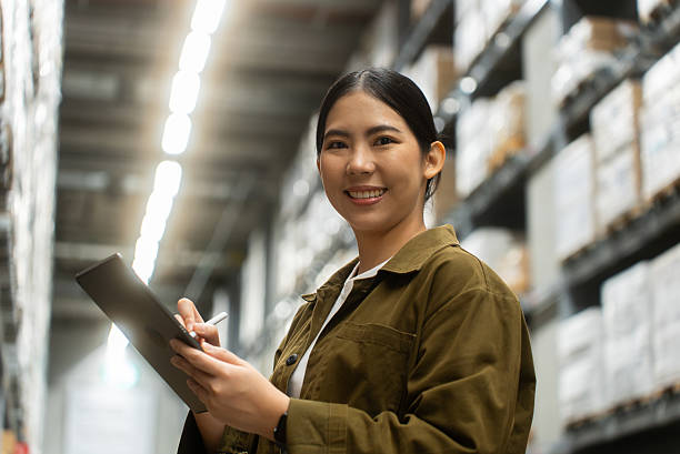 istock Portrait smiling confidently woman worker managing track inventory to fulfill data using smart digital tablet in logistics center with stacked shipping boxes and supply chain products in warehouse. 2226575370
