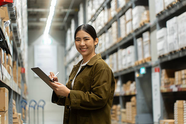 istock Portrait smiling confidently woman worker managing track inventory to fulfill data using smart digital tablet in logistics center with stacked shipping boxes and supply chain products in warehouse. 2226575371