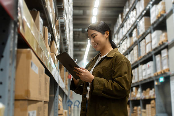 istock Portrait smiling confidently woman worker managing track inventory to fulfill data using smart digital tablet in logistics center with stacked shipping boxes and supply chain products in warehouse. 2226575393