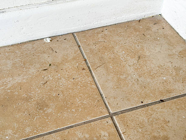 Stock photo shows a dirty tiled floor with brown stone-effect tiles, appearing heavily grubby and stained. The flooring is visibly messy and unhygienic, with accumulated dirt and grime across the surface
