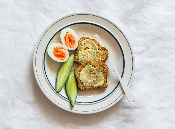 istock Delicious breakfast - toasts with butter, boiled egg, fresh cucumber on a plate on a light background, top view 2226579057