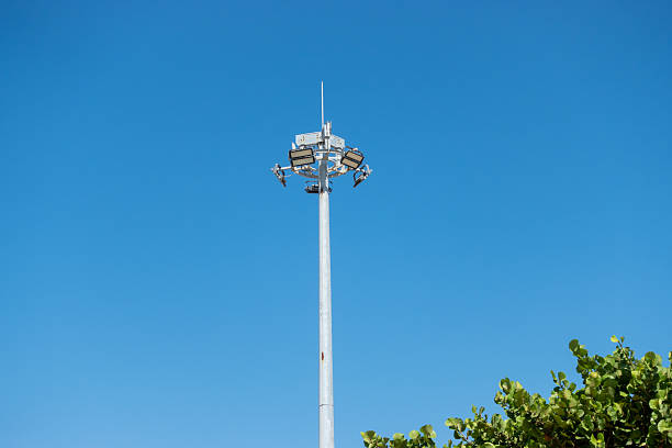 istock Tall stadium-style light pole against a clear blue sky with green tree leaves at the bottom 2226581228