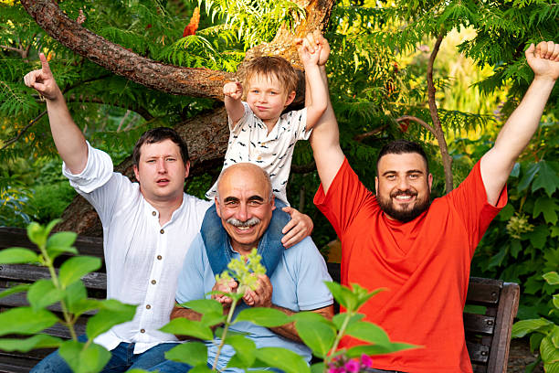 Elderly great-grandfather and three little great-grandchildren having fun with smart phone watch funny videos, enjoy new amusing mobile application at home. Multi-generational people using modern tech