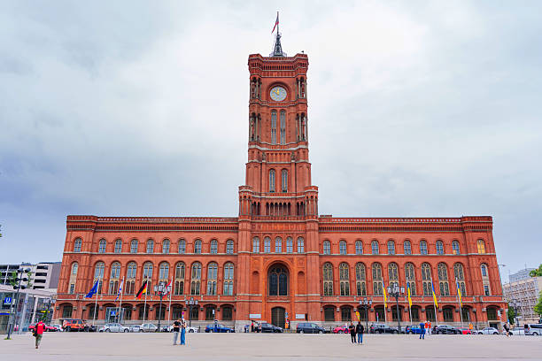 Berlin, Germany - June 1, 2025: Prominent Red City Hall in Berlin featuring striking architecture and intricate details, surrounded by flags and a cloudy sky, creating a dramatic urban scene.