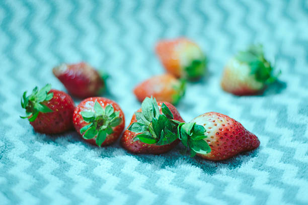 Ripe strawberries arranged on a teal chevron patterned textile. Close-up composition with shallow depth of field, highlighting juicy texture.