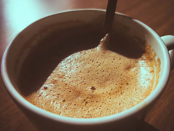 Close-up of frothy latte in a white mug, on a wooden table in a cafe setting, highlighting texture and light. Close-up of frothy latte in a white mug, on a wooden table in a cafe setting, highlighting texture and light. chocolate and coffee cafe stock pictures, royalty-free photos & images