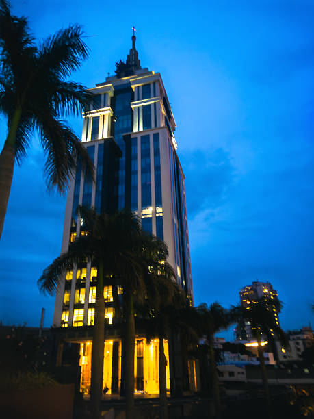 Illuminated UB City skyscraper at twilight, Bengaluru. Palm trees frame the modern mansion-like structure against the deep blue sky.