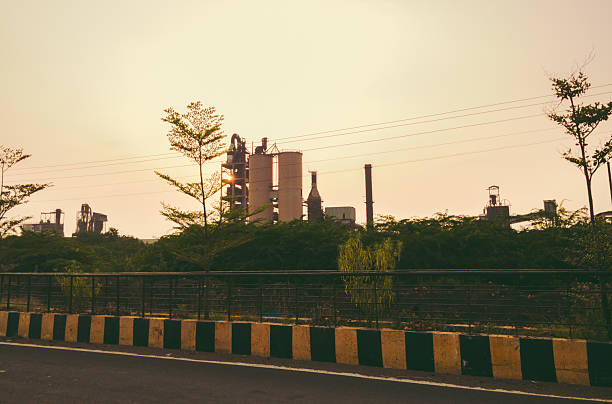 Cement Industrial factory silhouetted against a setting sun, viewed from a roadside in India, creating a striking composition.