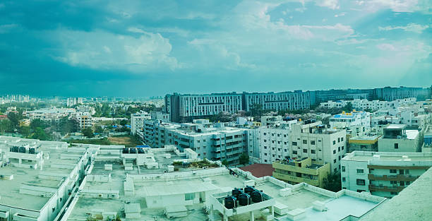Panoramic view of Bengaluru, India cityscape under a dramatic sky.  Multistory buildings and rooftops dominate the composition.