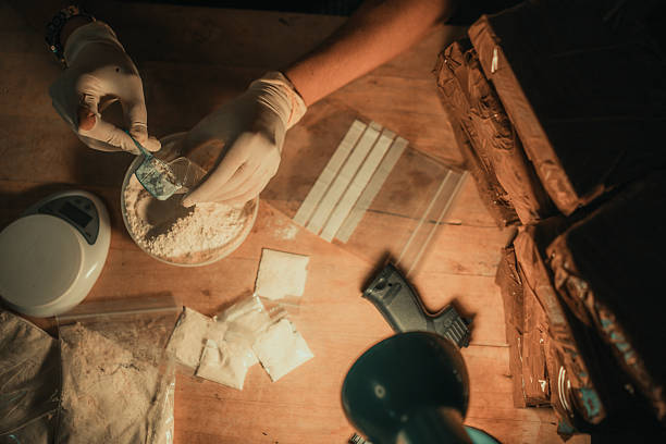 Hands preparing a powdered substance at a workspace with tools and packaging materials in view, suggesting an industrial or scientific context.