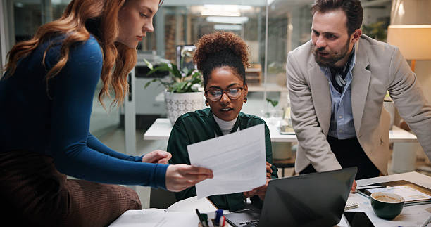 istock Business people, document and meeting in office for discussion, project feedback and advice at night. Journalist team, paper and tech in agency for article review, collaboration and late information 2226612812