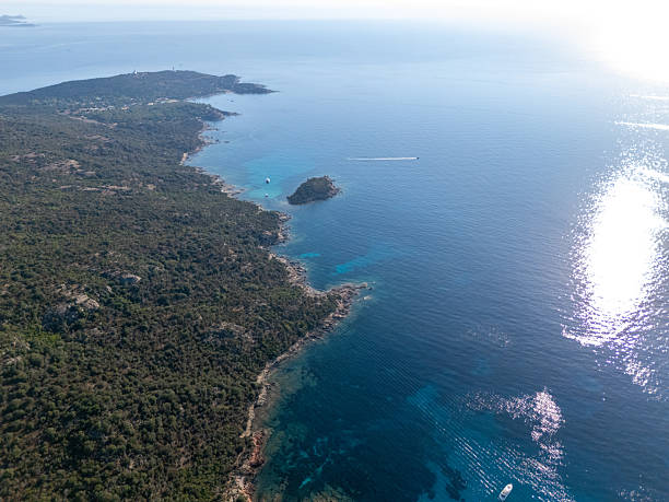 A small boat drifts in crystal-clear turquoise water near rocky coastlines. Aerial view shows calm sea and natural shoreline. Scenic ocean landscape with boat and coastal vegetation.
