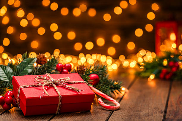 istock Red gift box under the Christmas tree in a cozy festive atmosphere with defocused string lights at background. Candy cane and ornaments 2226629192