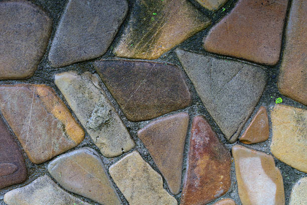 Multicolored smooth stones of irregular shape form a decorative surface, held together by mortar. Their natural texture and shades from brown to grey create an attractive and authentic pattern, ideal for a background.