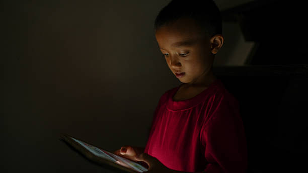 istock Child focused on tablet in dimly lit environment, showcasing curiosity and engagement with technology. soft glow from screen highlights child features, creating serene atmosphere 2226633340