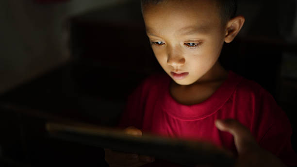 istock Focused child engages with tablet, illuminated by its screen in dimly lit environment, showcasing curiosity and concentration 2226633349