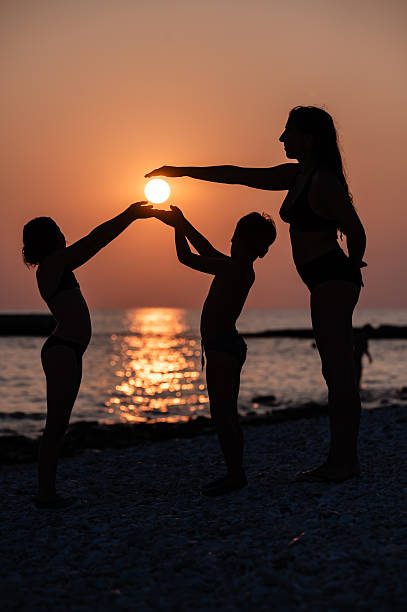 Silhouetted family joyfully holding the glowing sun in their hands while enjoying a beautiful beach at sunset, creating cherished memories