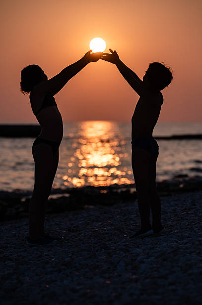 Two children holding the setting sun in their hands, creating a beautiful silhouette against the orange sky