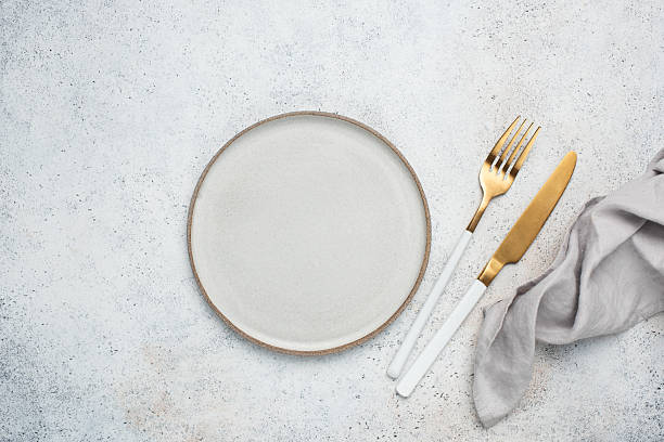 Food background, table setting: Empty grey plate, golden cutlery and table cloth on grey stone backdrop, top view copy space