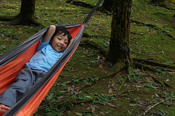A young boy lying in a hammock with arms behind his head, enjoying a peaceful moment in the forest.