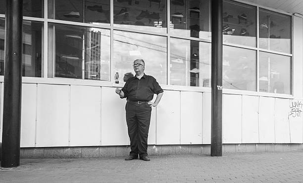 Kyiv, Ukraine - 20th July,2025: Middle-aged male employee smoking a cigarette during his work break, standing outside the shoe store where he works, in black and white