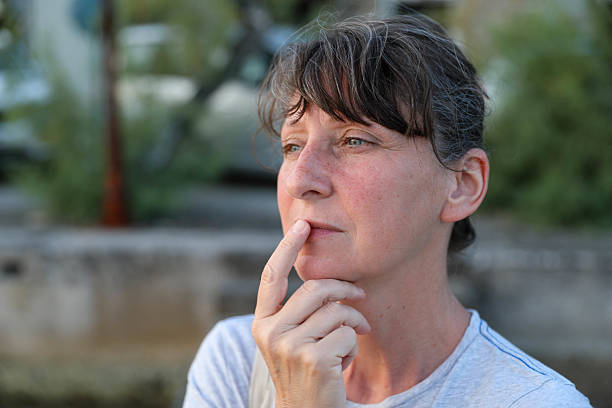 Portrait of a Thoughtful Mature Woman Touching Her Lips While Gazing into the Distance, Reflecting in a Peaceful Outdoor Setting