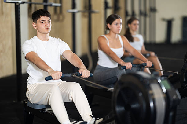 Young athletic guy in sportswear training on rowing machine in gym