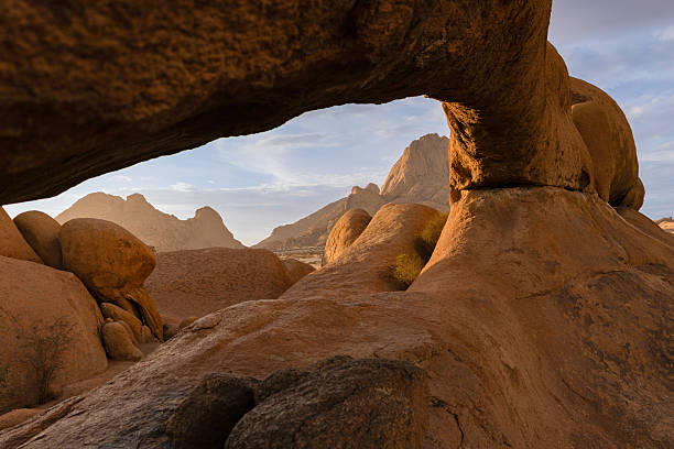 Scenic view of spitzkoppe mountain range through natural rock arch at sunrise, namibia, africa