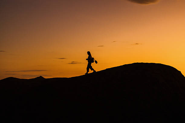 Silhouette of a young woman walking up a hill at sunset
