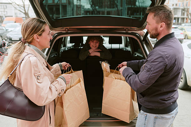 Parents seen packing groceries in car trunk while smiling child sits in backseat enjoying the moment. Family bonding during outdoor shopping trip